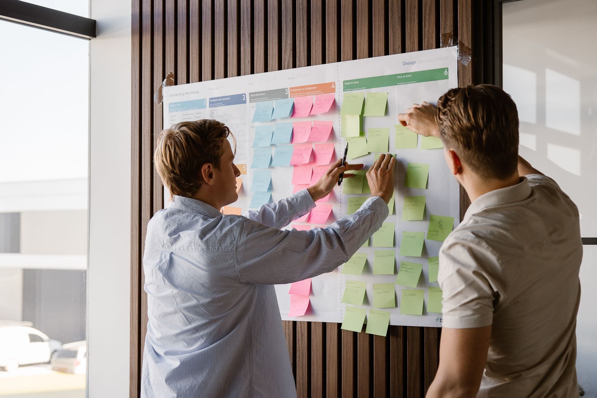 Twee productontwikkelaars van Brisk verdelen eisen en wensen voor een programma van eisen over de kolommen Need to have en Nice to have van een workshopposter