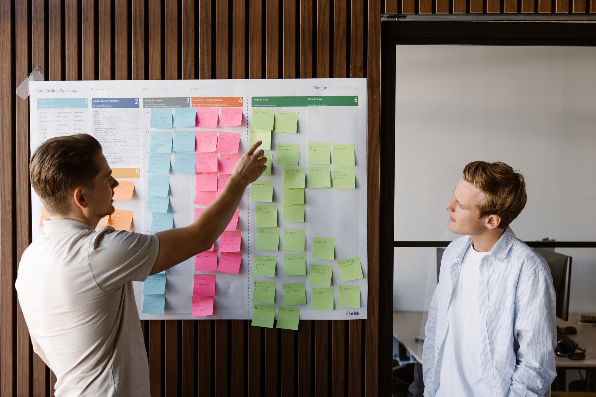 Twee productontwikkelaars van Brisk werken de eerste fase van productontwikkeling uit op een workshopposter met de stappen van Design, Develop en Deliver